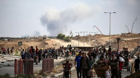 AFP عبر Getty Images يرتفع عمود من الدخان في الخلفية مع عودة الفلسطينيين من نقطة توزيع الطعام التي تديرها مجموعة مؤسسة غزة الإنسانية المدعومة من الولايات المتحدة والمدعومة الإسرائيلية.